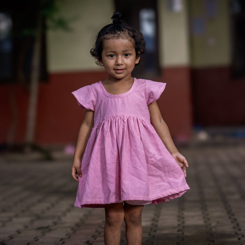 Young girl in a pink dress standing on a paved area with a blurred background
