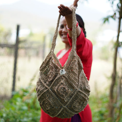 Woman holding a woven bag outdoors with greenery in the background